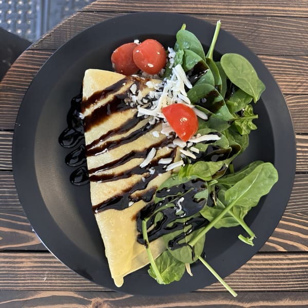 Savory crepe drizzled with balsamic glaze, topped with cheese, cherry tomatoes, and a side of spinach.