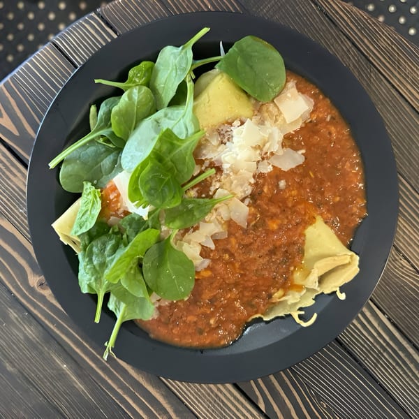 Savory crepes with tomato sauce, spinach, avocado, and shaved cheese on a dark plate.