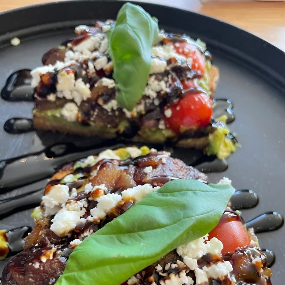 Two savory crepes topped with feta, tomatoes, basil, and balsamic glaze on a black plate.